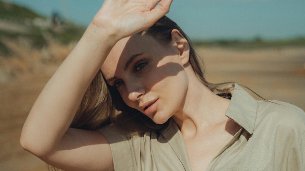 A young woman shielding her eyes from the sun on a sandy beach.