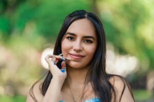 Portrait of a young woman with paint on her hand, smiling outdoors in natural setting.