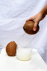 A hand pours fresh coconut water into a glass on a white background.