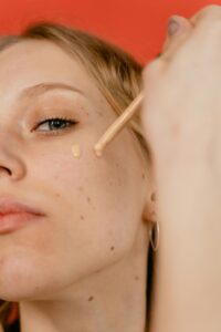 A close-up shot of a woman applying liquid foundation to her face with a dropper.