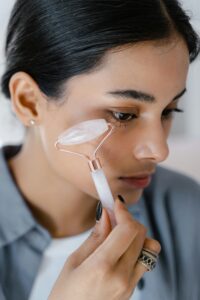 Woman applying jade roller for facial skincare, promoting self-care and beauty routines.